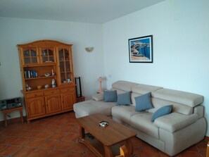 A living room with a beige sofa, a wooden cabinet, a framed picture on the wall, and a tiled floor.