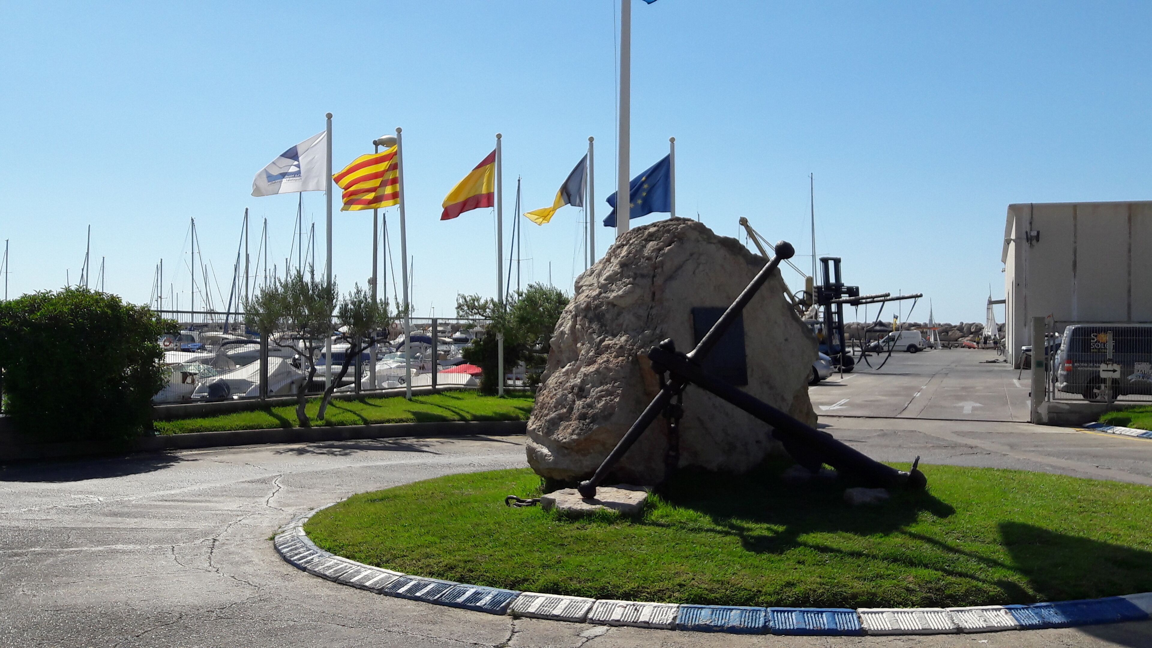 A marina with multiple flags, a large rock sculpture, and boats.
