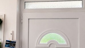 Une porte blanche avec un vitrage dépoli, un climatiseur VIVAX fixé au-dessus, et un interrupteur fixé au mur sur le côté gauche.