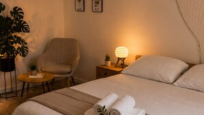 Une chambre à coucher avec un lit, une chaise, une table de chevet avec une lampe, une plante et un tableau au mur.