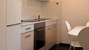 Une cuisine compacte avec des meubles blancs, une hotte noire, un évier en acier inoxydable et une table à manger blanche avec deux chaises.