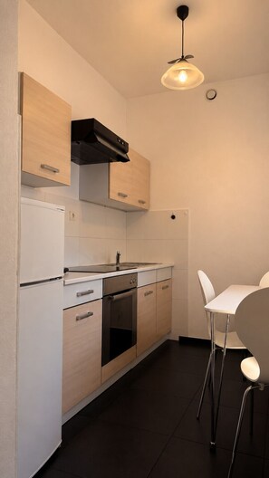 A compact kitchen with white cabinetry, a black range hood, a stainless steel sink, and a white dining table with two chairs.