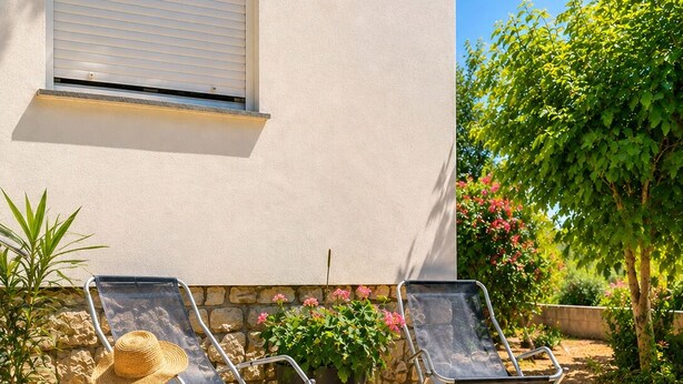 Une terrasse avec deux fauteuils de jardin, une plante en pot et un mur en pierre.