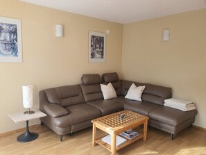 A living room with a brown sectional sofa, a small wooden coffee table, a white lamp, and two framed pictures on the wall.