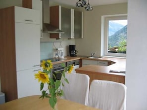 A kitchen with a view of mountains, a dining table with chairs, and a vase with sunflowers.