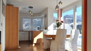 Une cuisine moderne avec des meubles en bois, un coin repas avec des chaises blanches et une grande fenêtre donnant sur les montagnes.
