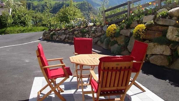 Une terrasse avec une table et des chaises, un mur de pierre orné de fleurs et une vue sur les montagnes.