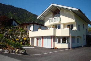 A two-story building with a balcony, a parking area, and a mountainous backdrop.