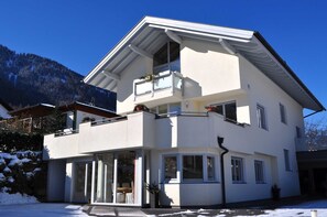 A two-story building with a balcony, large windows, and a mountain backdrop.