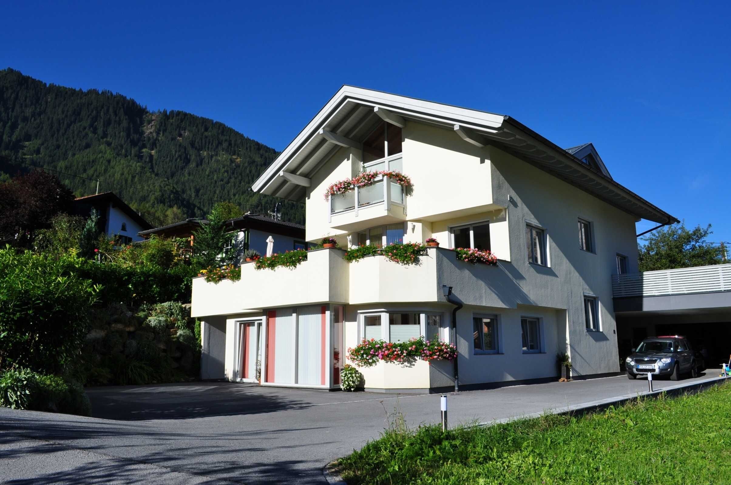 A two-story building with a balcony, a garage, and a mountain backdrop.