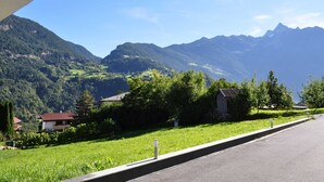 Une route de campagne bordée de maisons et de verdure, offrant une vue sur un paysage montagneux.