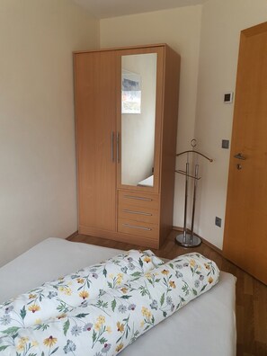 A bedroom with a wooden wardrobe, a bed with floral bedding, and a bedside table with a lamp.