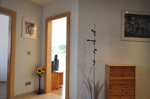 A room with a wooden cabinet, a framed picture, a tall plant, and a doorway leading to another room. - Apartment Wilhelm (Sautens)