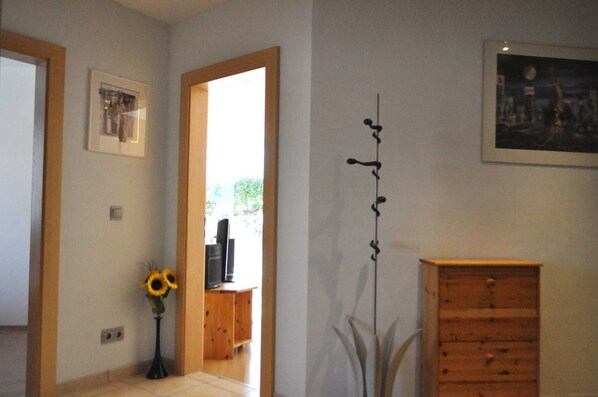 A room with a wooden cabinet, a framed picture, a tall plant, and a doorway leading to another room.