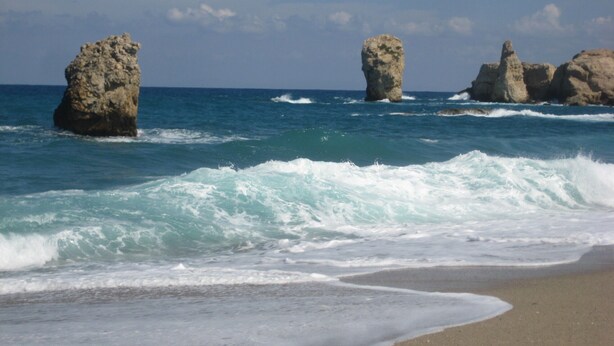 Una playa con olas y formaciones rocosas.