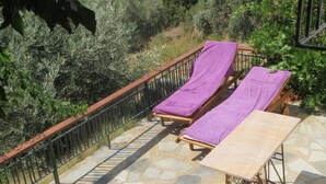 Una terraza con dos tumbonas cubiertas con toallas moradas, suelo de piedra y barandilla de metal.