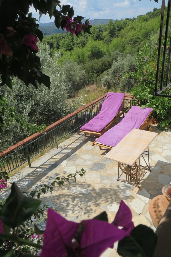 A terrace with two sun loungers covered with purple towels, a stone floor, and a metal railing.