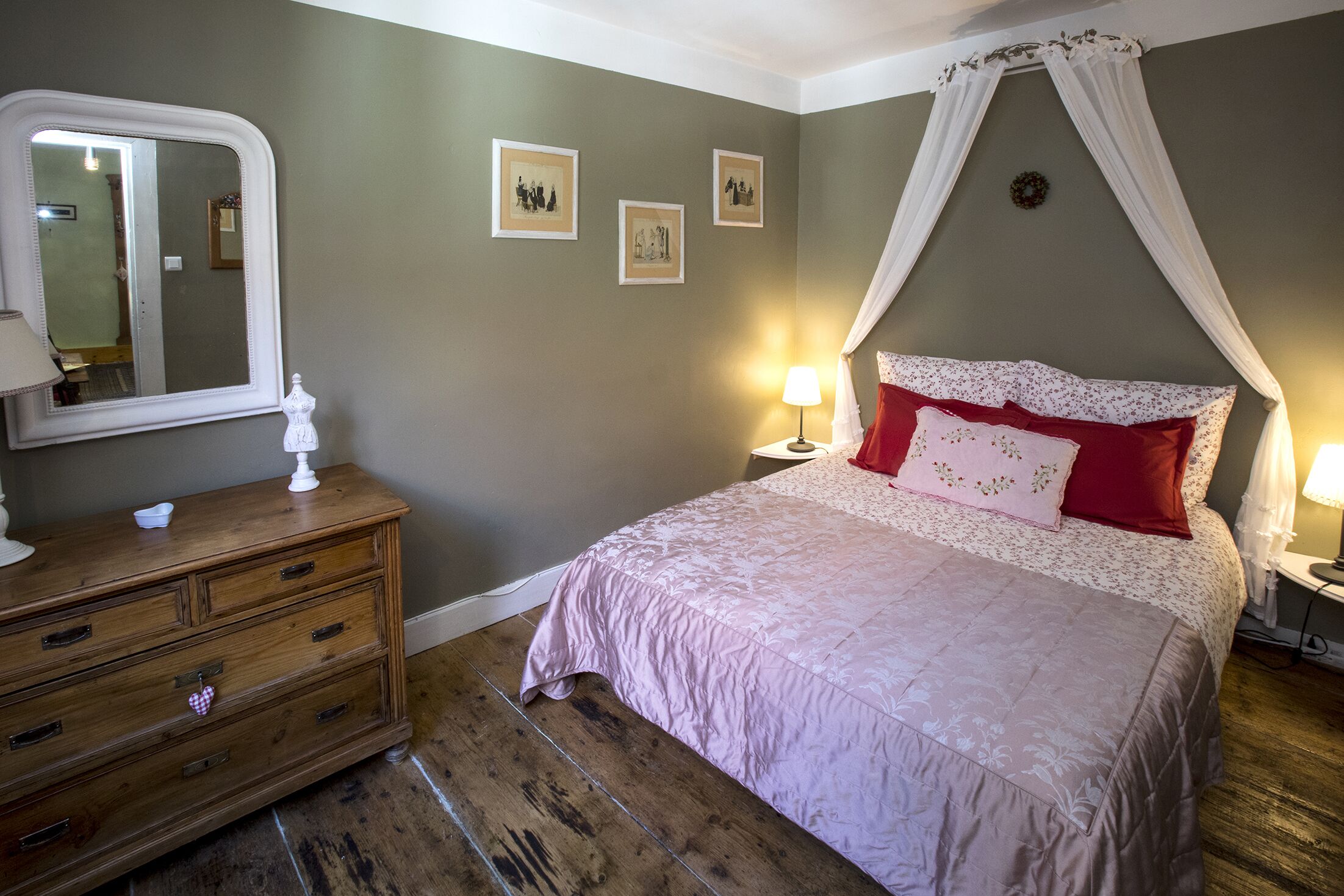 A bedroom with a bed, a dresser, a mirror, and wall-mounted picture frames.