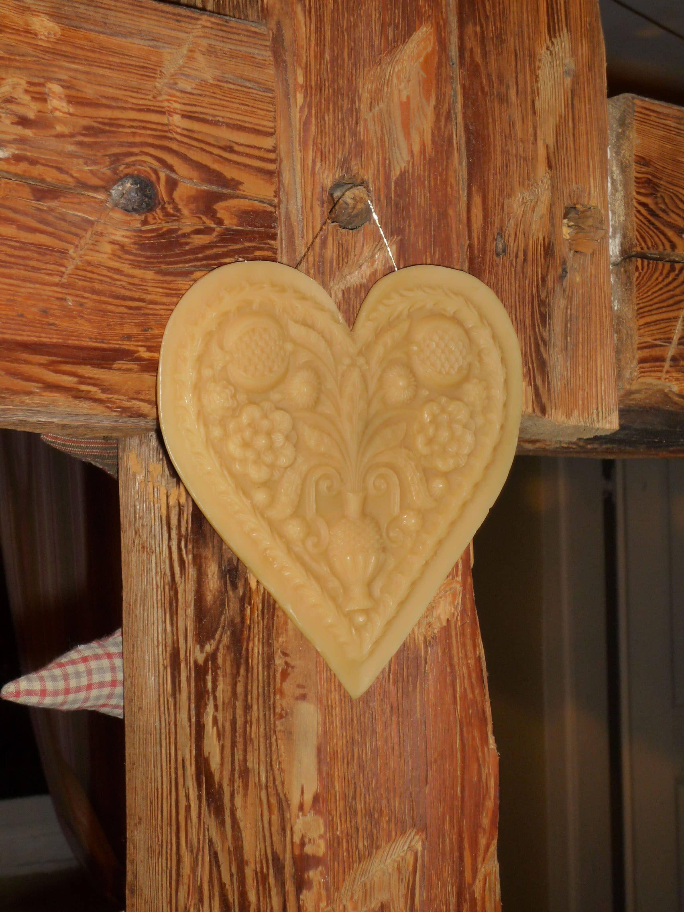 Ein herzförmiges dekoratives Element mit floralen und fruchtigen Schnitzereien, auf einer Holzkonstruktion befestigt.