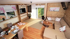 A cozy living area with a wooden floor, a sofa, a dining table set for four, and a television. - Fantastic vacation apartment VANESSA in an idyllic location in the Zittau Mountains (Oybin)