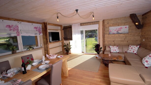 A cozy room with a wooden ceiling, a dining table set for four, a sofa, and a television. - Fantastic vacation apartment VANESSA in an idyllic location in the Zittau Mountains (Oybin)