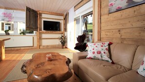 A cozy living room with a wooden coffee table, a beige sofa, and a flat-screen TV mounted on the wall. - Fantastic vacation apartment VANESSA in an idyllic location in the Zittau Mountains (Oybin)