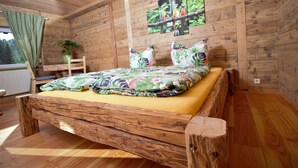 A wooden cabin-style bedroom with a bed, a window with curtains, and a wall-mounted picture. - Fantastic vacation apartment VANESSA in an idyllic location in the Zittau Mountains (Oybin)