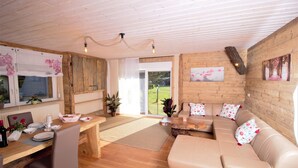 A cozy living room with a wooden floor, a sofa, a dining table with chairs, and a fireplace. - Fantastic vacation apartment VANESSA in an idyllic location in the Zittau Mountains (Oybin)