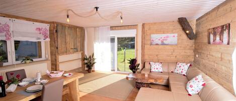 A cozy living room with a wooden floor, a sofa, a dining table with chairs, and a fireplace.