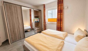 A hotel room with a bed, a wardrobe, a television, and a window with curtains.