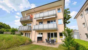 Ein mehrstöckiges Wohngebäude mit Balkonen, einem Grillplatz und einer kleinen Terrasse mit Stühlen.