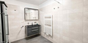 A modern bathroom with a glass shower enclosure, a black vanity with a mirror, and a white towel rack. - Apartment AS04 - Villa hill (Heringsdorf)