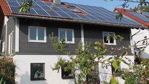 Een huis met twee verdiepingen, zonnepanelen op het dak en een kleine tuin ervoor.
