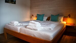 Een net opgemaakt tweepersoonsbed met witte lakens en teal kussens, een houten hoofdbord en twee bedlampjes.