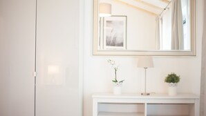 A white wardrobe, a mirror with a decorative frame, a lamp, and two potted plants on a white console table. - New: Luxurious apartment with lake view & garden [Nr. 2] (Storkow (Mark))