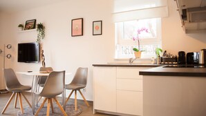 A modern kitchen with a dining area, white cabinetry, a flat-screen TV, and a potted orchid by the window. - New: Luxurious apartment with lake view & garden [Nr. 2] (Storkow (Mark))