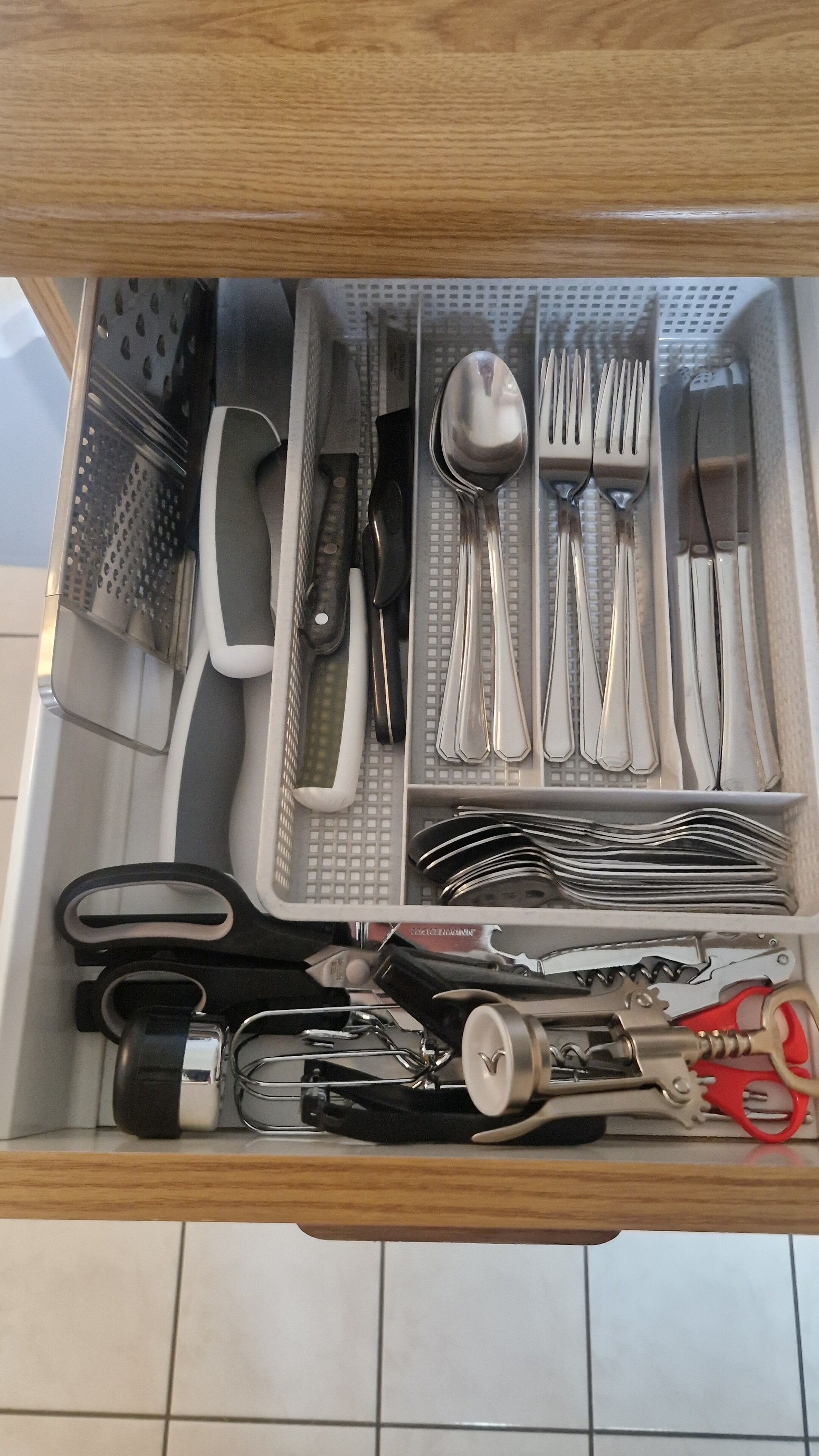Un tiroir contenant des ustensiles de cuisine bien rangés, notamment des couteaux, des cuillères, des fourchettes et une râpe.