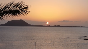 Une plage au coucher du soleil, avec une mer calme et des montagnes à l’horizon.