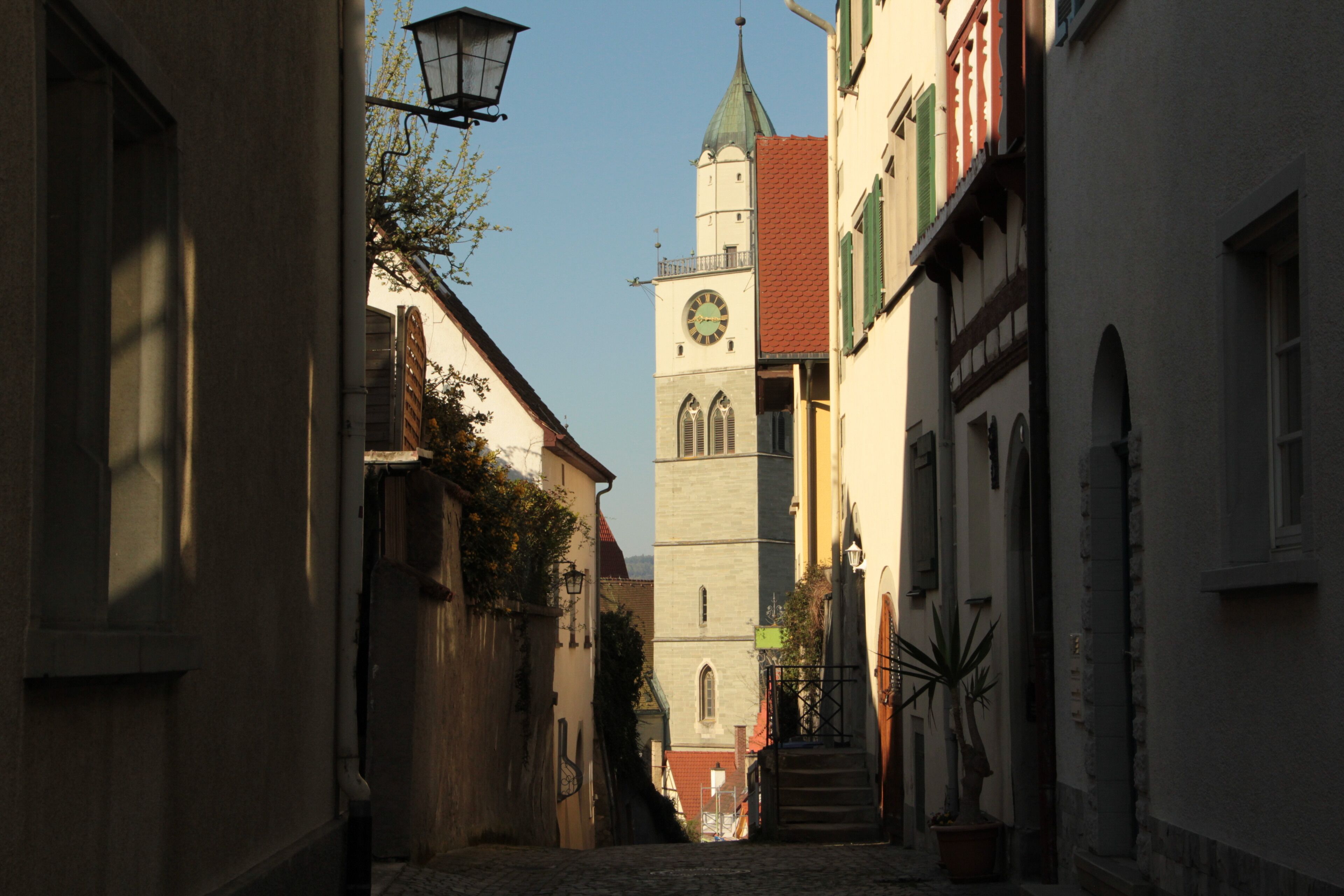 Une rue étroite bordée de bâtiments historiques, avec un beffroi et un pavé de pierres.