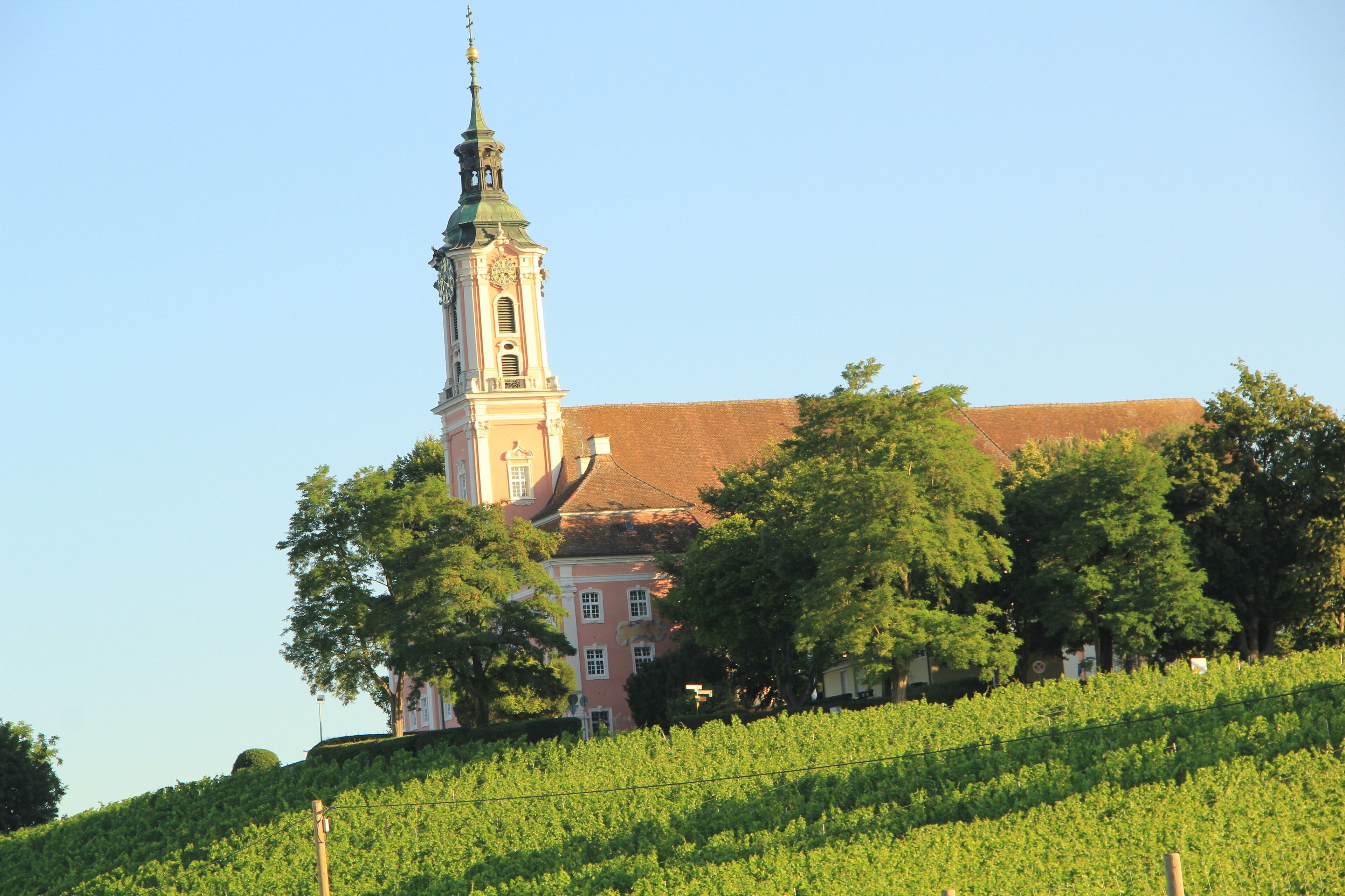 Ein Gebäude mit einem markanten Turm und einem roten Dach, umgeben von üppiger Vegetation.