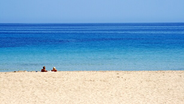 Uma praia com águas azul-claras e areal arenoso.