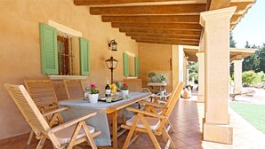 Um pátio externo com mesa e cadeiras de madeira, toldos verdes e piso de azulejos.
