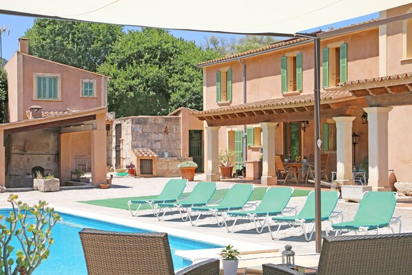 A poolside area with lounge chairs, a swimming pool, and a building with green shutters.