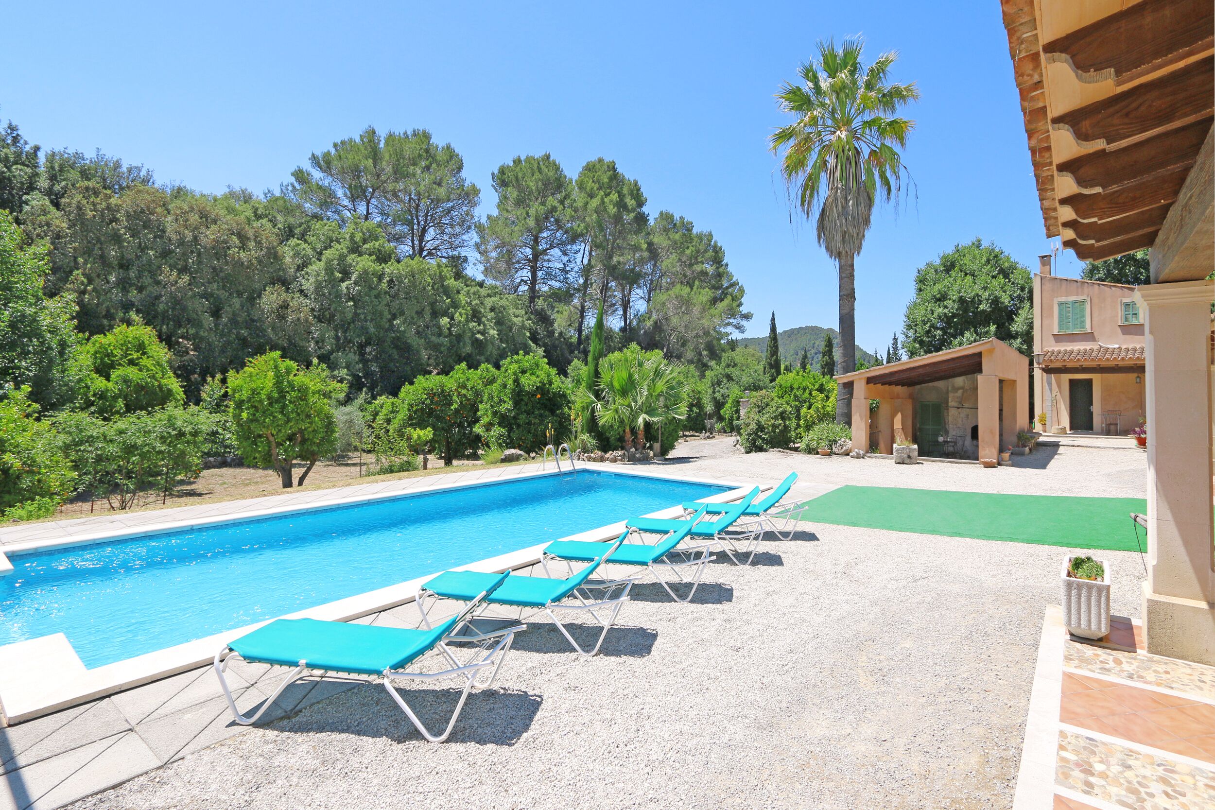 Una piscina con lettini, circondata da alberi e un edificio con tetto in tegole.