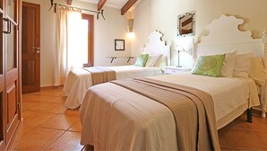 Quarto com duas camas, porta de madeira, janela com cortinas e luminária fixada na parede.