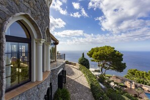 A stone building with large windows and a balcony overlooking a coastal view. - ****** Villa Valldemossa ****** (Valldemosa)