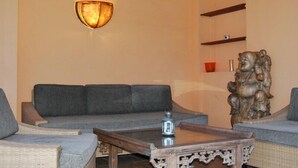 Ein Wohnzimmer mit grauem Sofa, einem Holztisch, einer wandmontierten Leuchte und einer dekorativen Holzskulptur.