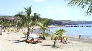 Ein Strand mit Palmen, badenden Personen und freiem Blick aufs Meer.
