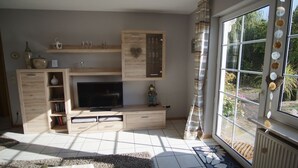 A living room with a TV, wooden cabinets, and a large window. - Beautiful vacation rental in Bitburg-Stadt, with its own outdoor relaxation area (Bitburg)