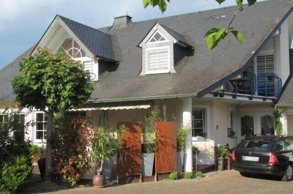 A two-story house with a sloped roof, a front porch with potted plants, and a parked car. - Beautiful vacation rental in Bitburg-Stadt, with its own outdoor relaxation area (Bitburg)
